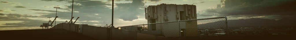 Picture of a building with cranes, mountains, and clouds in the background.